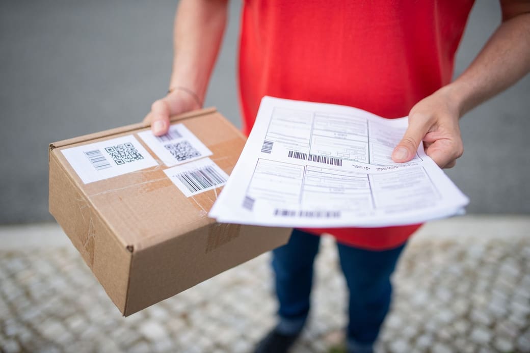 Hands holding out a barcoded parcel and its shipping paperwork
