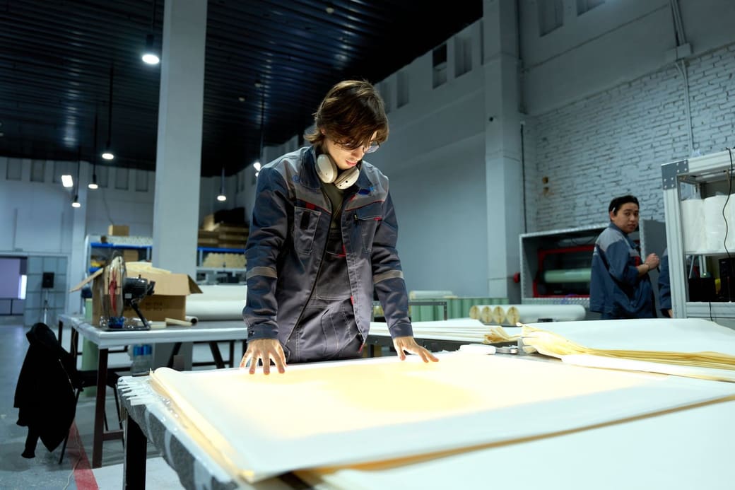 A worker in a factory hall leaning over a table to check a stack of large printed sheets