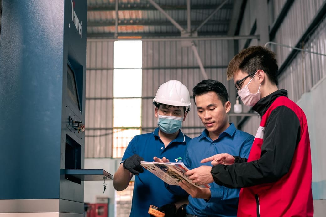 Three supply chain staff, one in a hard hat, going over a printed plan together on a warehouse floor