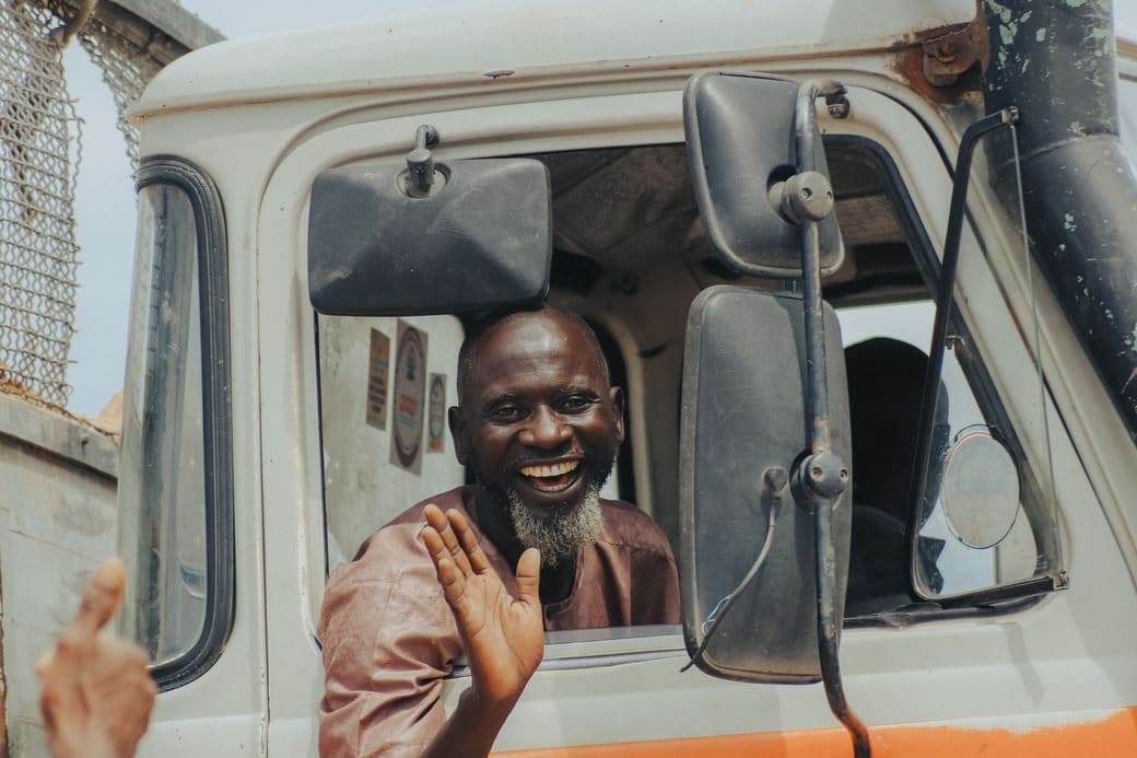 A smiling truck driver waving from the cab window of his truck