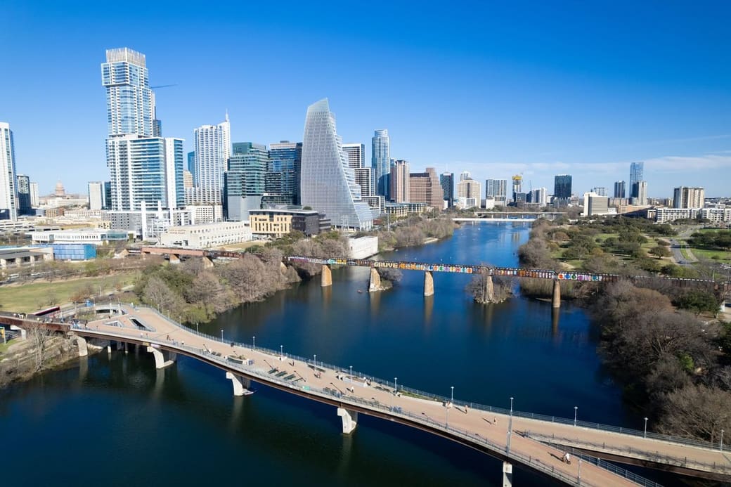An aerial view of a downtown of glass towers above a wide river crossed by several bridges, with parkland along the banks