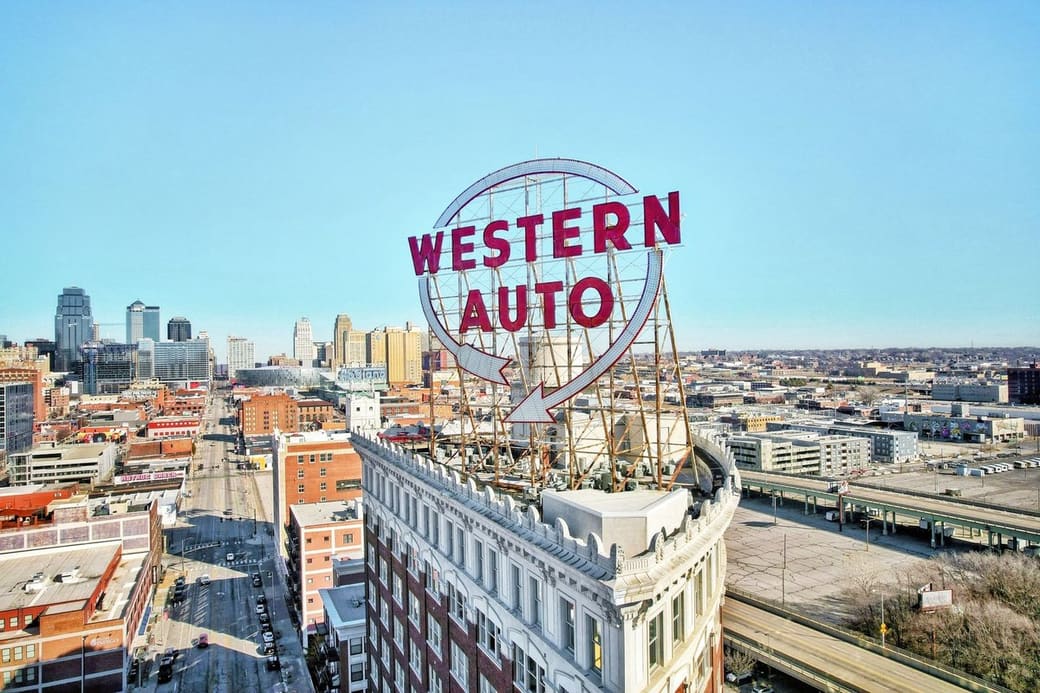 A large red rooftop sign reading Western Auto on a curved white building, with a downtown skyline and highways behind under a clear sky