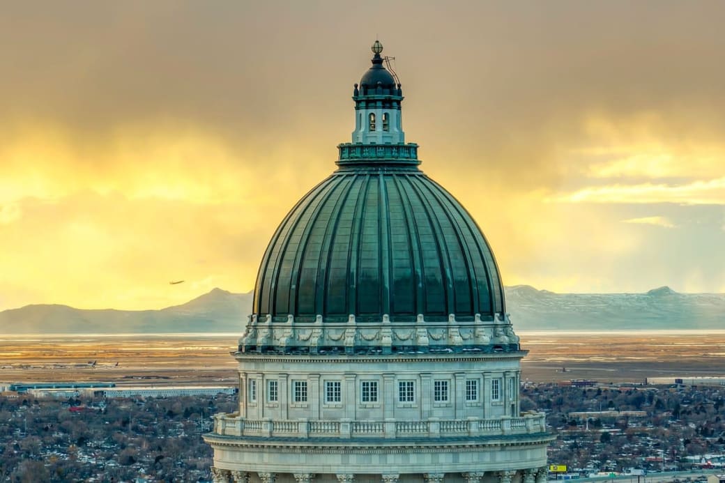 A green copper dome on a neoclassical capitol building at sunset, with a mountain range on the horizon behind it