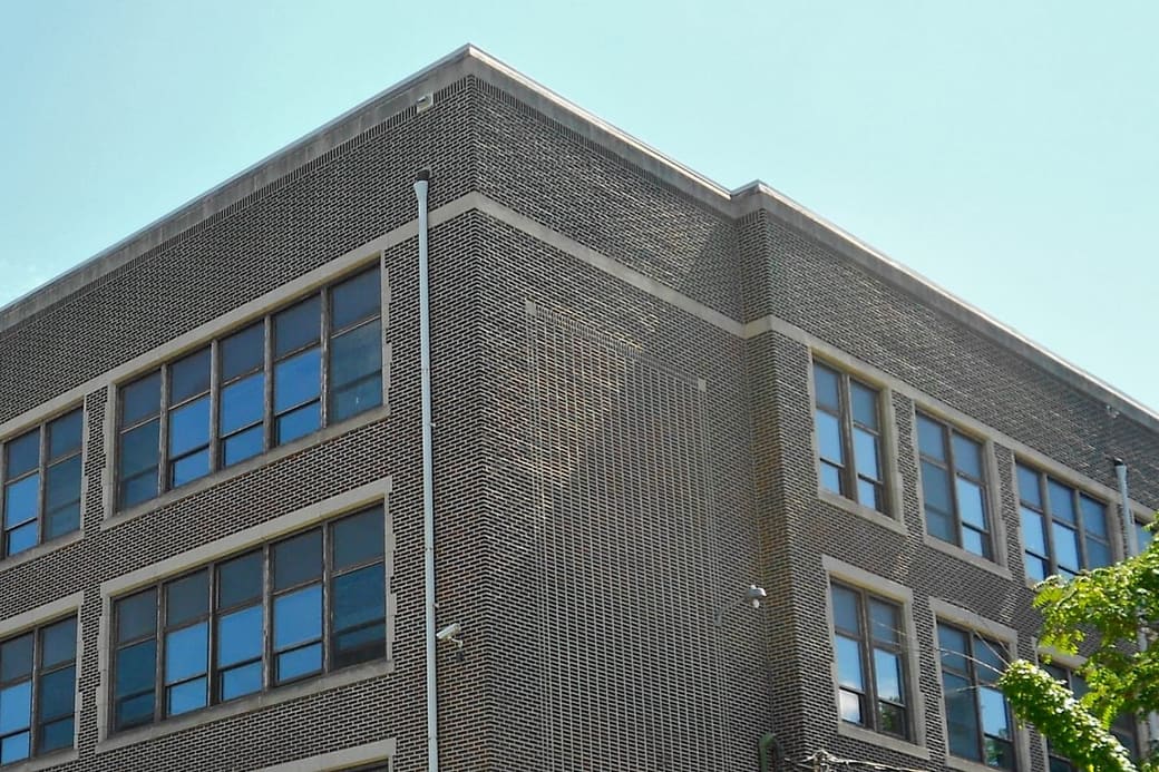 The brick corner of a 1930s civic building, patterned brickwork between deep window bays, against a pale blue sky