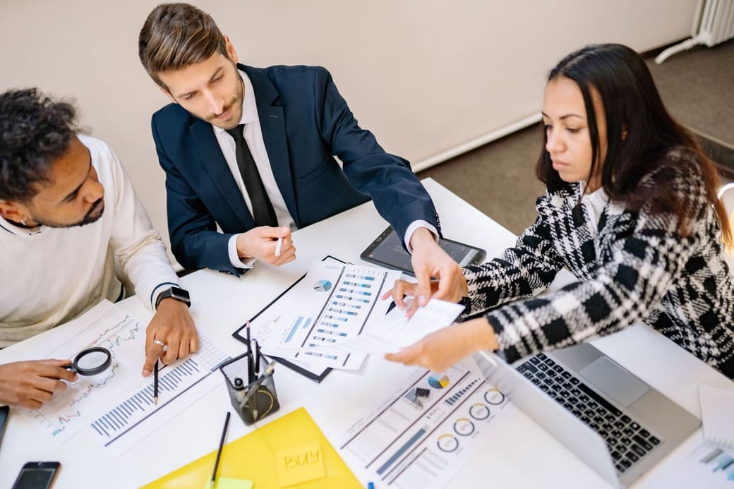 Four colleagues around a table working through printed charts and a laptop in a planning meeting