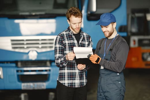 Two men checking paperwork beside a truck, for the online logistics degrees ranking