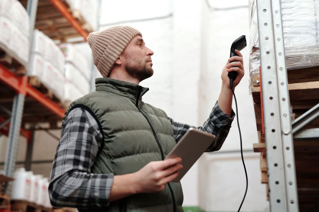 A warehouse worker holding a tablet and scanning a barcode on a high storage rack