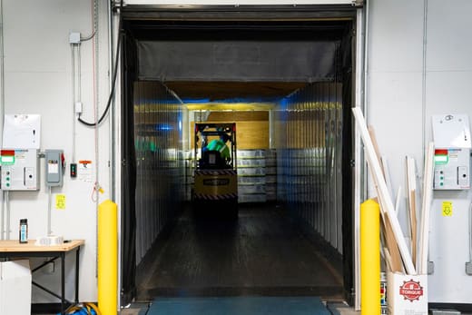 A forklift loading pallets into a trailer at a dock door
