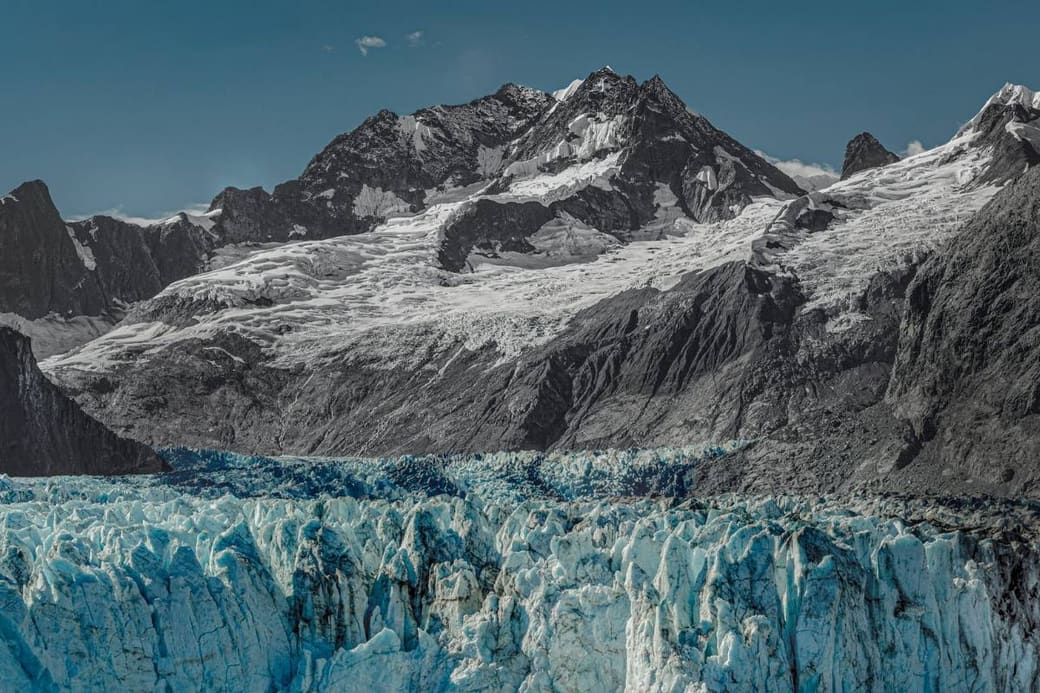 A glacier front meeting the sea below dark snow-streaked mountains