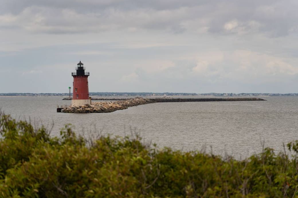 A red and white lighthouse at the end of a long stone breakwater under gray cloud