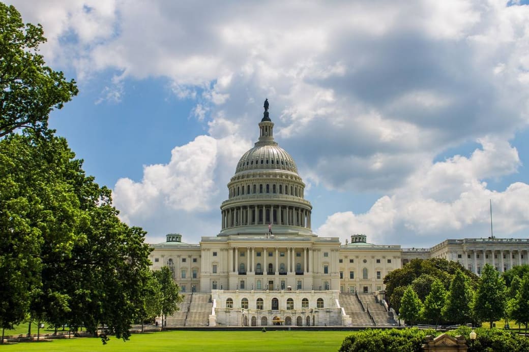 The domed United States Capitol behind its lawn and trees under a bright sky