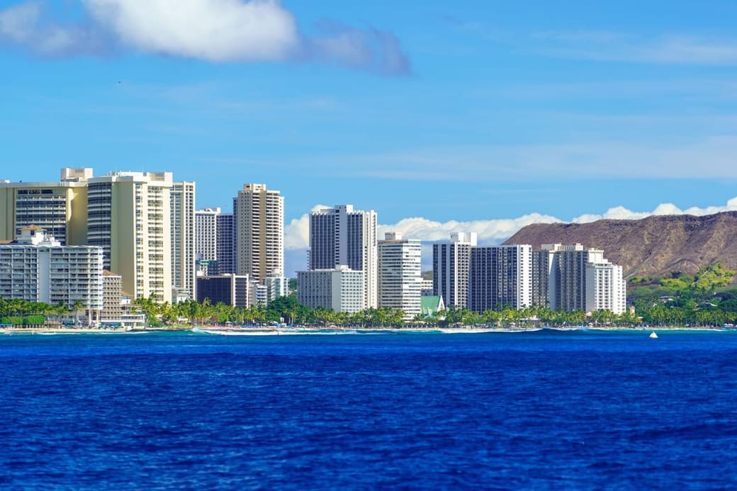 High-rise towers along a shoreline with a broad volcanic crater rising behind them
