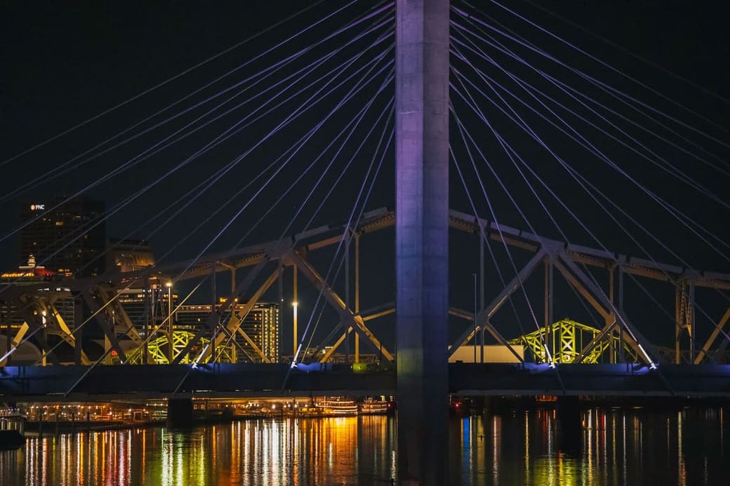 A lit cable-stayed bridge over a river at night with a city glowing behind it