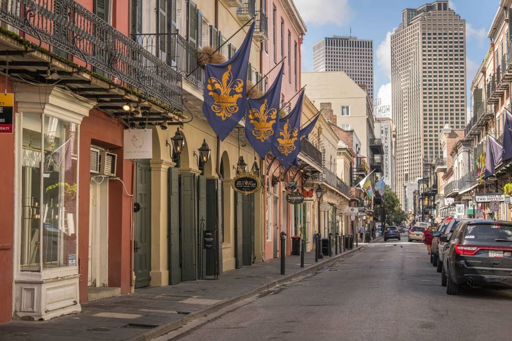 A narrow street of balconied townhouses with flags out, towers rising behind