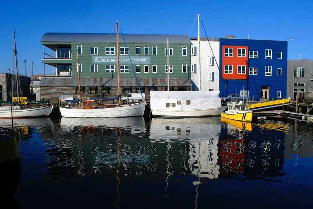 Boats moored along a working waterfront in front of low brick and timber buildings
