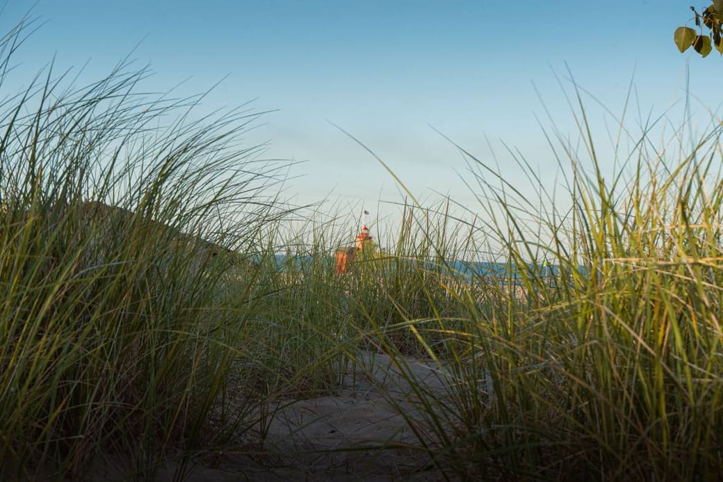 A red lighthouse seen through dune grass across a channel