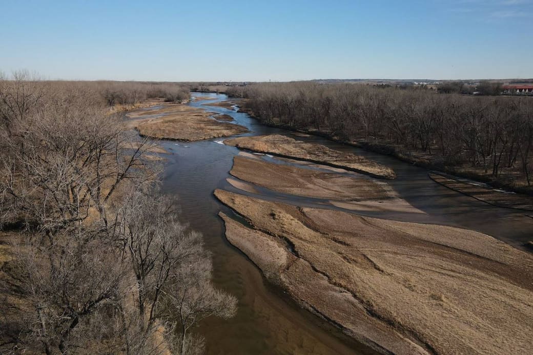 A wide braided river running through flat grassland under a big sky