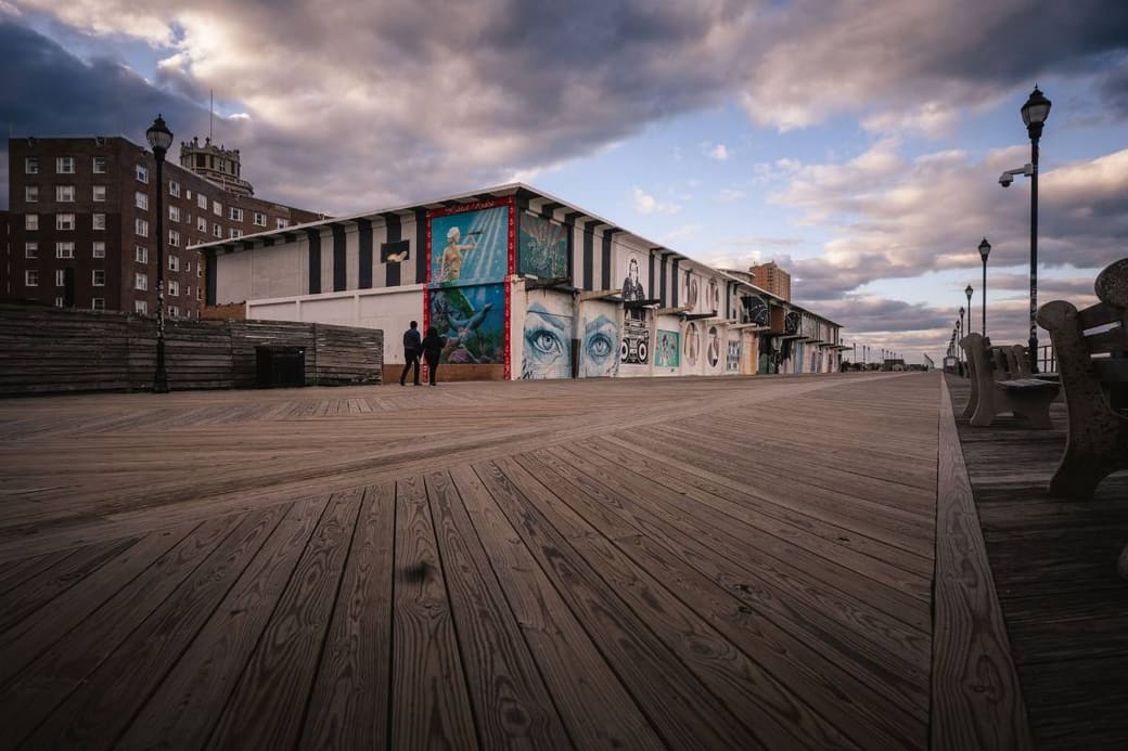 An empty timber boardwalk beside a mural-painted pavilion under a dramatic sky