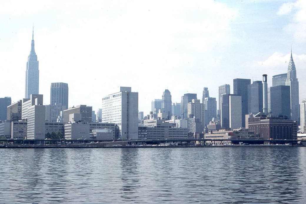 A dense skyline of skyscrapers along a waterfront under a pale sky
