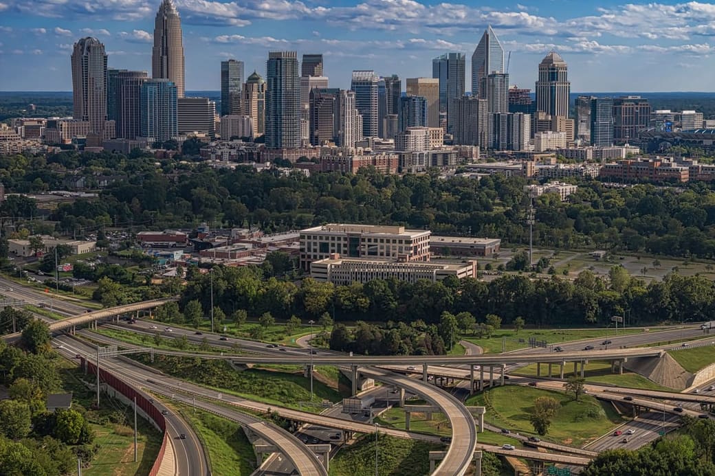 A cluster of glass towers above a green city, highways curving in the foreground