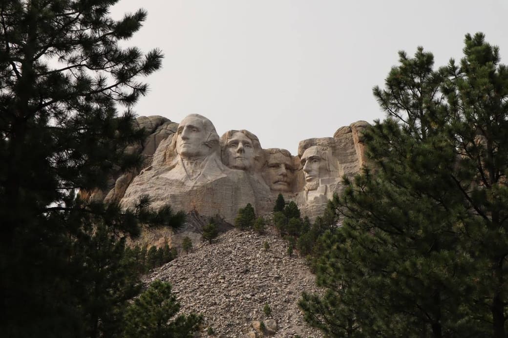 Four presidential faces carved into a granite mountain above pine trees
