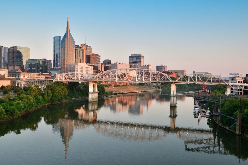 A skyline and a girder bridge reflected in a still river at sunrise